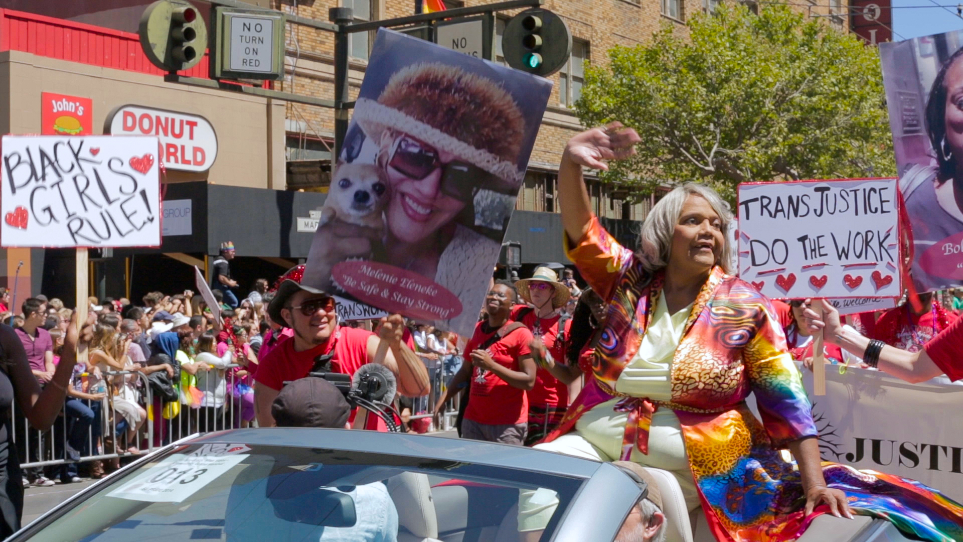 Miss Major sits in convertable car and waves to the crowd in a Pride parade