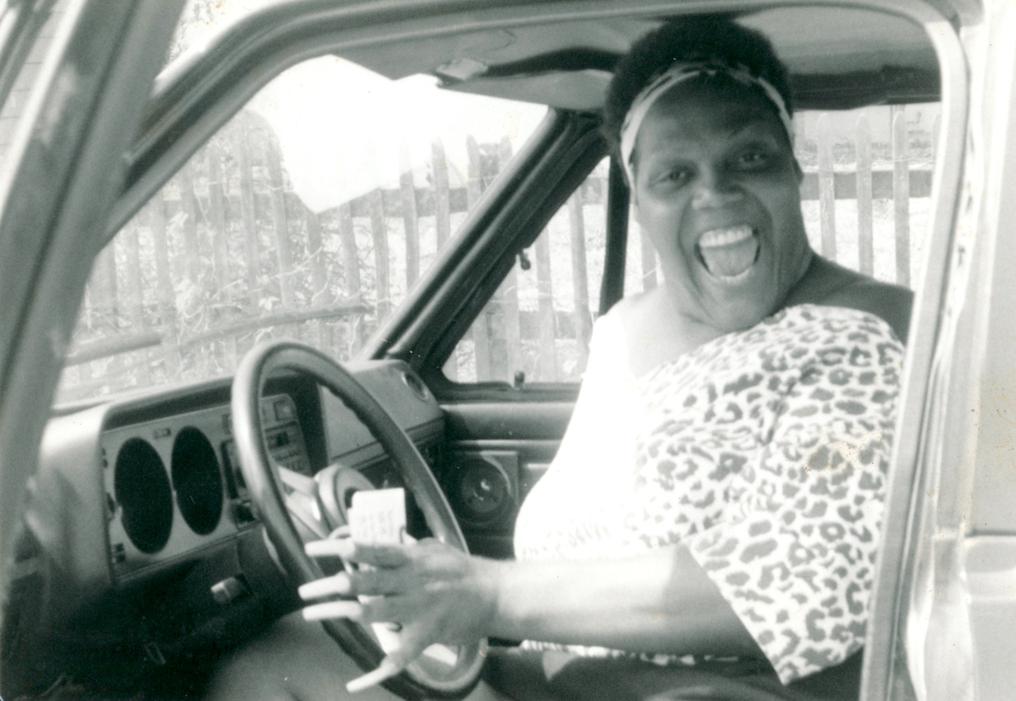Black and white photo of Miss Major in the drivers seat, flashing a big smile, with the car door open.